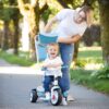 Mama potiska otroka na modro-belem triciklu po cesti.