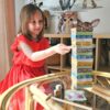 Deklica se igra z barvito stolpno igro iz naravnih materialov – razvija ravnotežje in natančnost