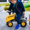 Otrok potiska rumen traktor JCB na igrišču.