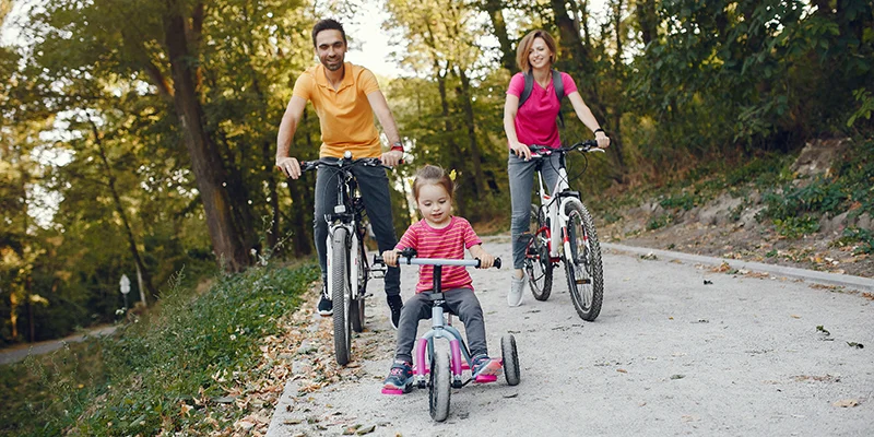 Družina na kolesarskem izletu v naravi – otrok na triciklu, starša na kolesih