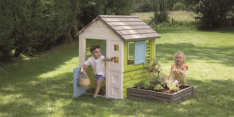 otroci se igrajo ob otroški vrtni hiški z gredico na travniku